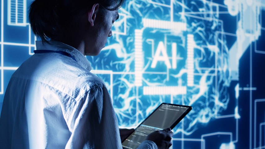 Immagine di repertorio, tecnico osserva un tablet, sullo sfondo un grande schermo con il logo AI