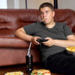 Adolescente sovrappeso, mangia cibo spazzatura mentre gioca ai videogame