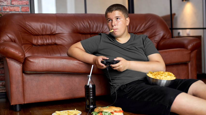 Adolescente sovrappeso, mangia cibo spazzatura mentre gioca ai videogame